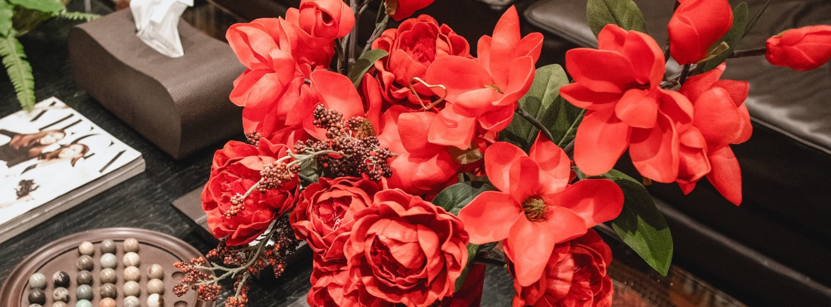 Red flowers in a decorative vase are displayed on a simple table.