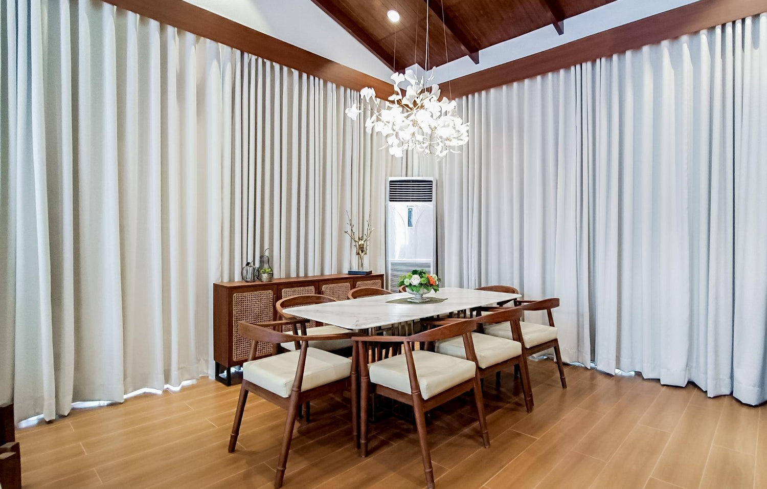 Elegant dining room with a wooden table, chairs, chandelier, and floor-length curtains.