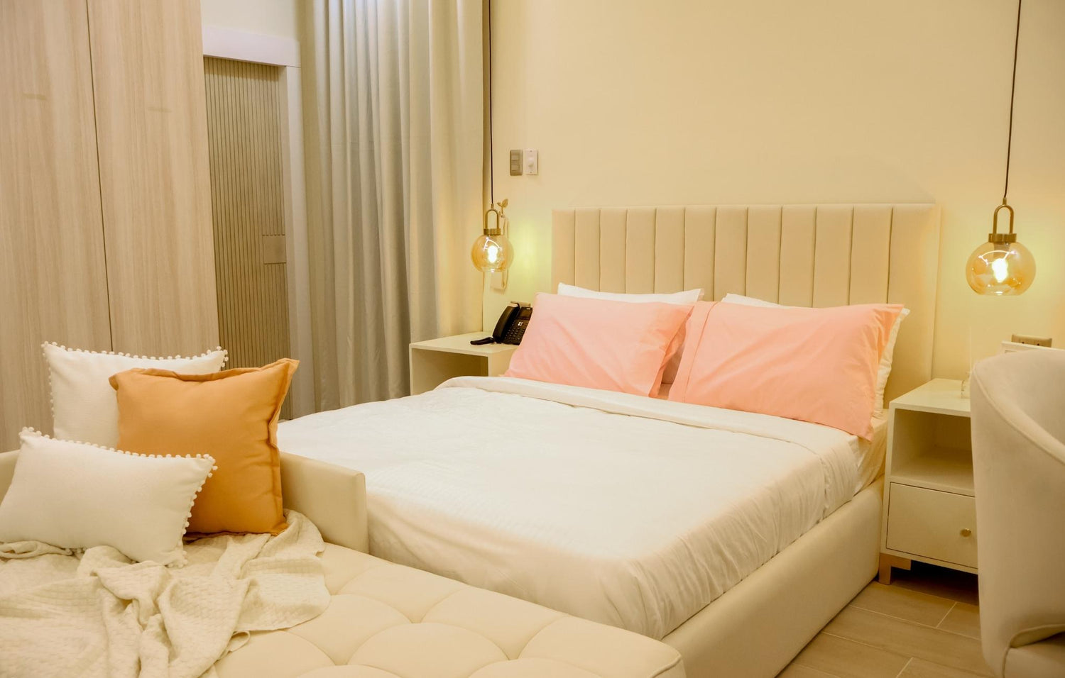 Cozy bedroom featuring a white bed adorned with soft pink pillows, creating a warm and inviting atmosphere.
