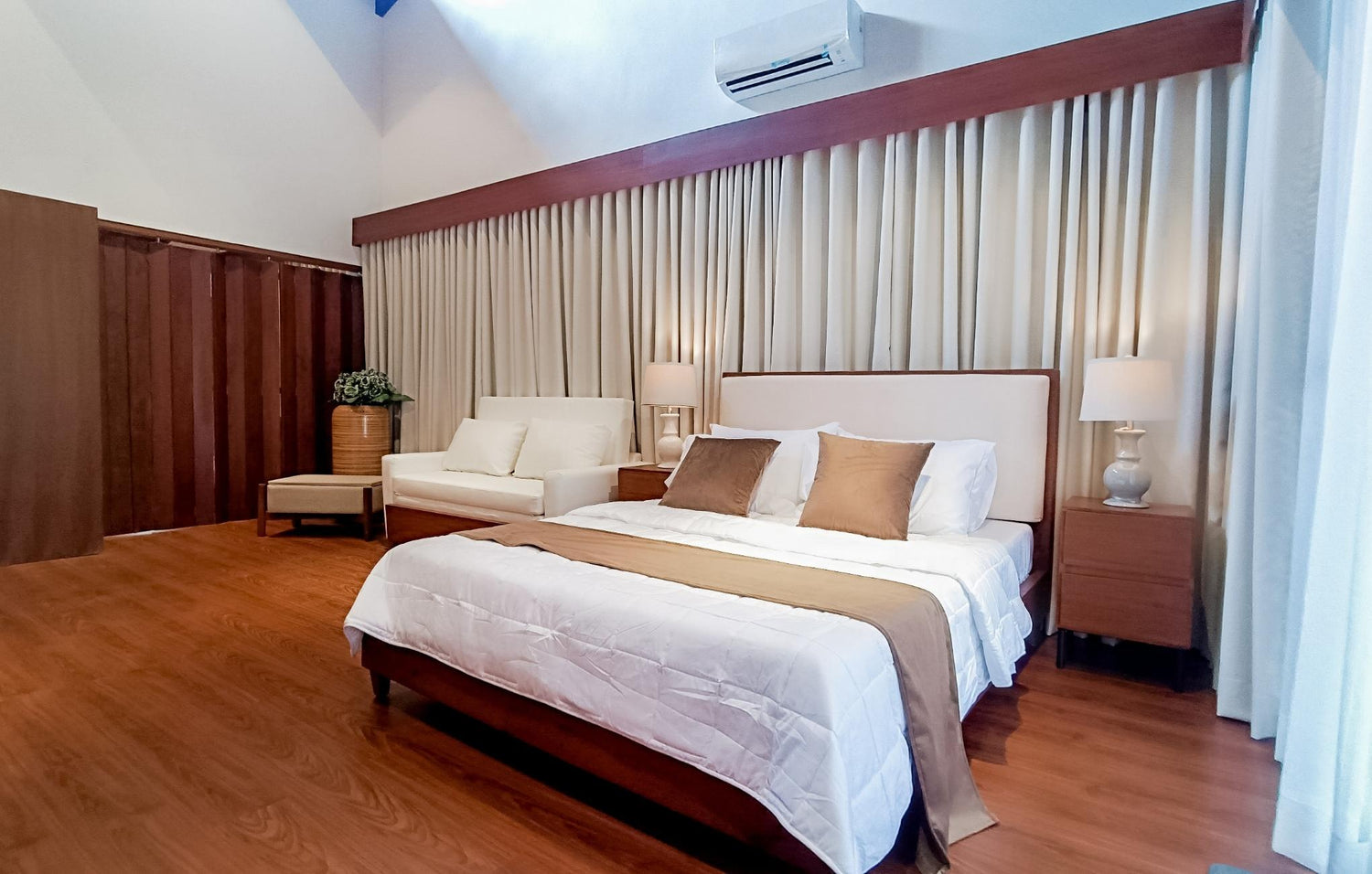 A cozy bedroom with a large bed, white and beige linens, a sofa, and wooden floors.