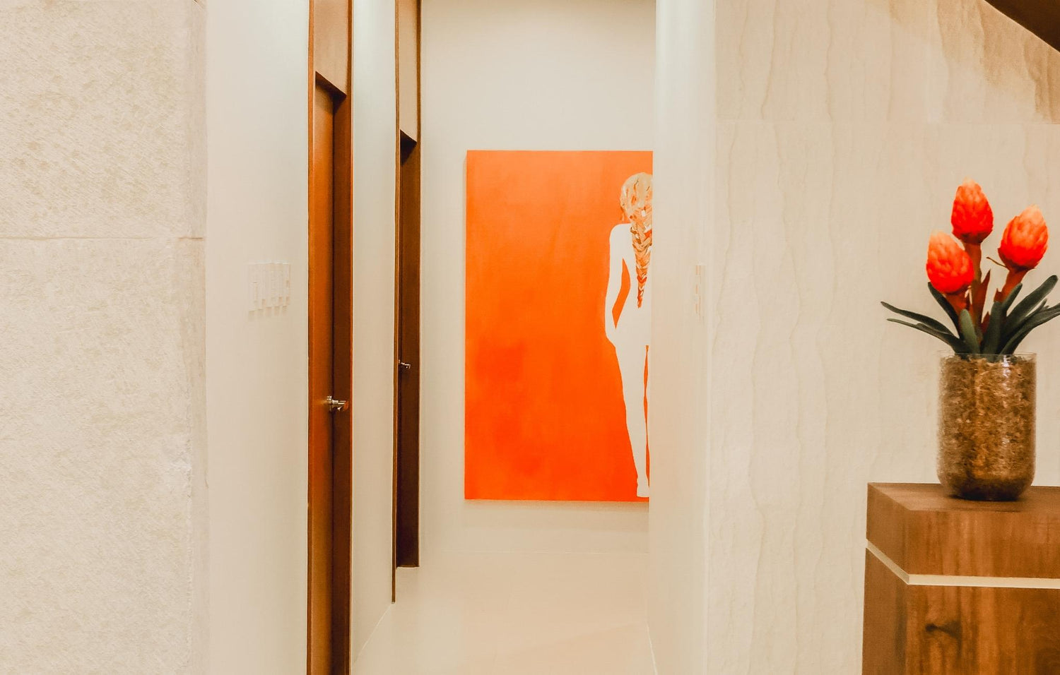 A hallway featuring a colorful painting on the wall and a vase filled with fresh flowers on a table.
