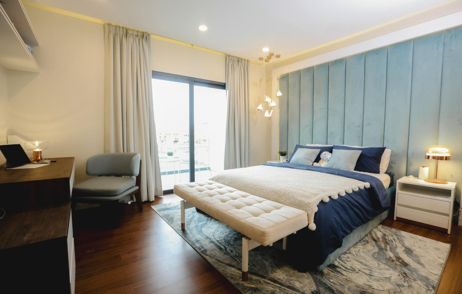 A cozy bedroom featuring a blue and white bed, complemented by soft lighting and minimalistic decor