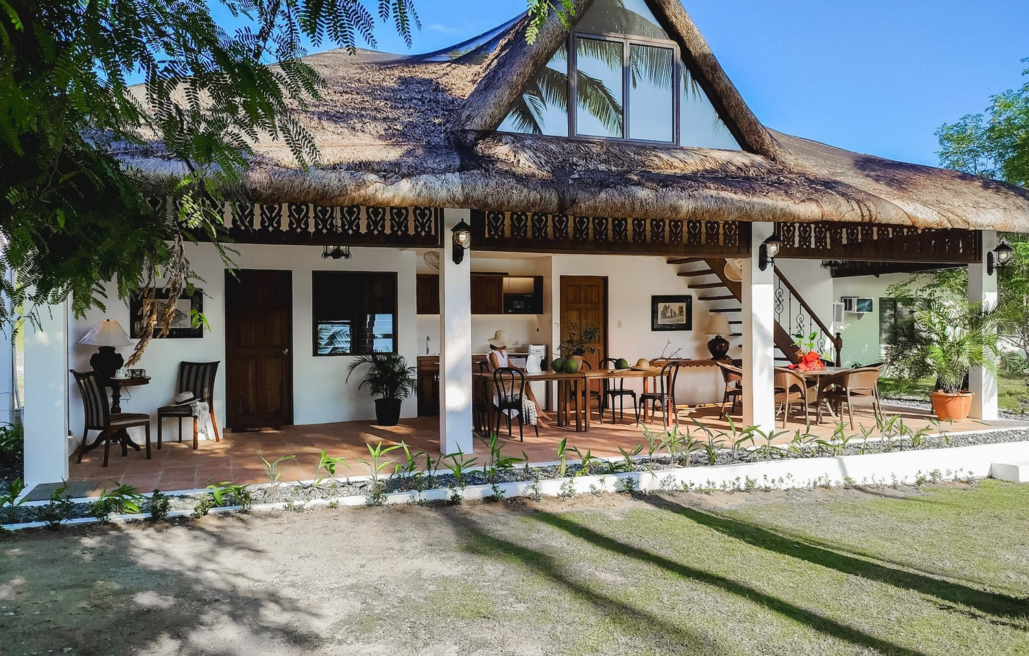 Thatched-roof house with open patio and dining set under a blue sky.
