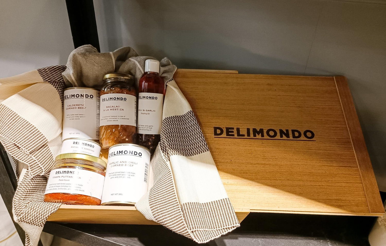 Wooden box with "DELIMONDO" branding, containing gourmet food products and a striped cloth.