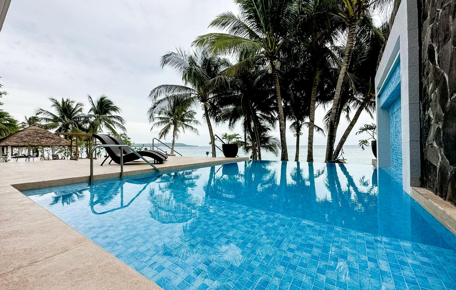 Infinity pool with lounge chairs overlooking a beach with palm trees.