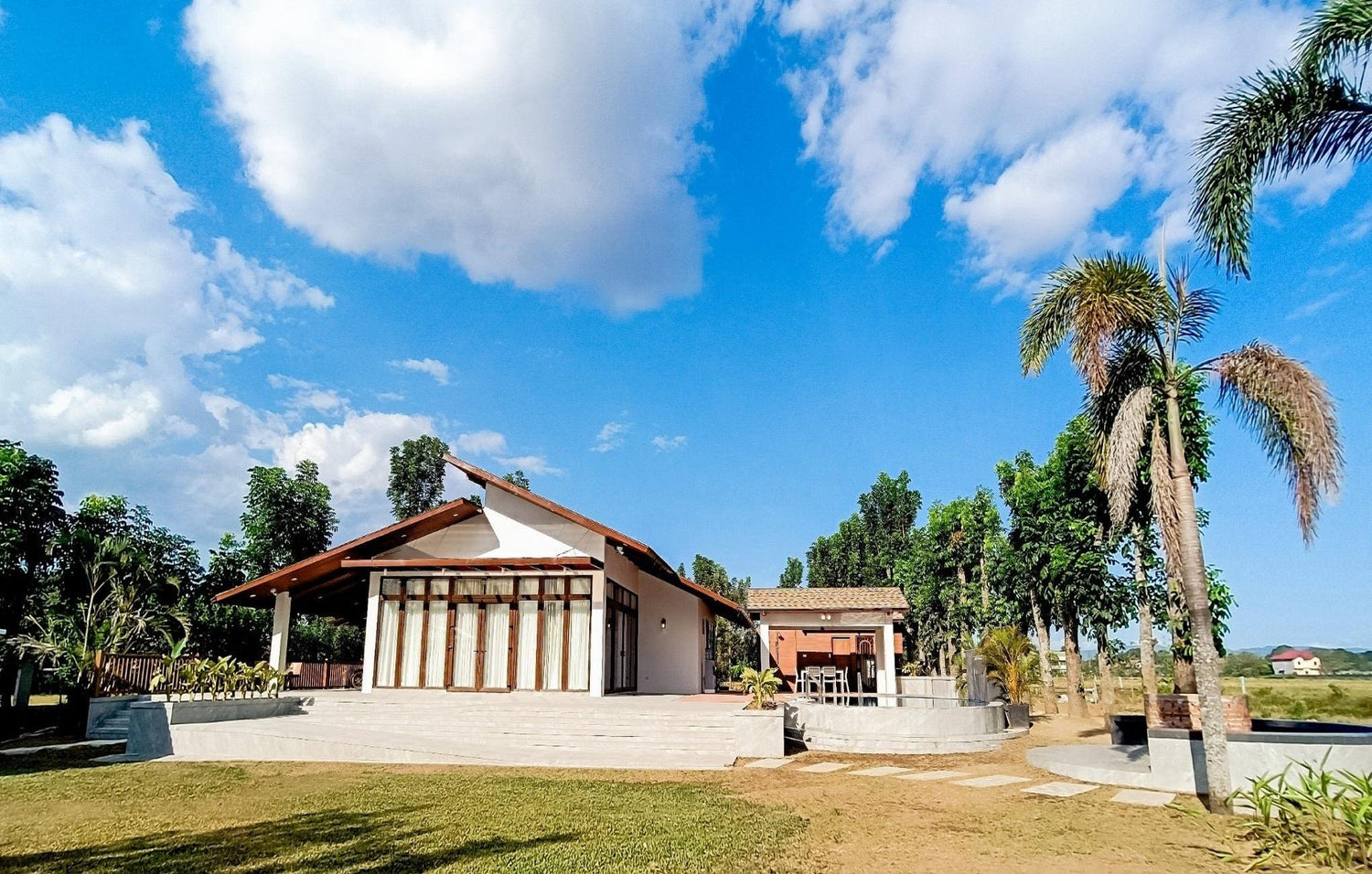 Rural house with veranda, palm trees, and clear blue sky.