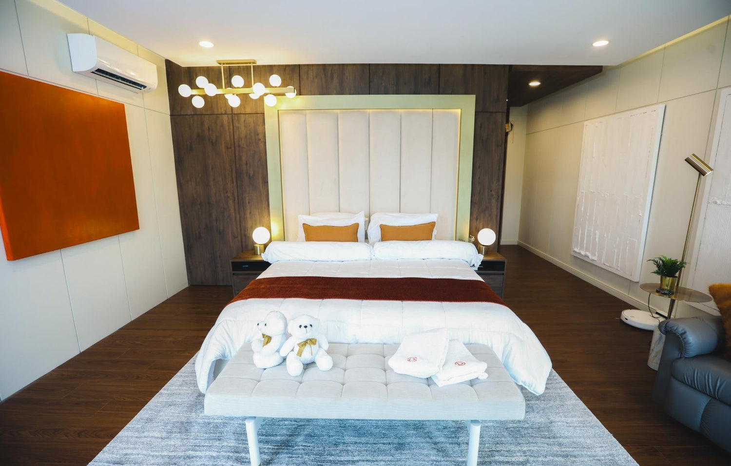 Luxurious bedroom featuring a tufted headboard, bold orange accents, a cozy throw, modern lighting fixtures, and a comfortable seating area with warm decor elements.
