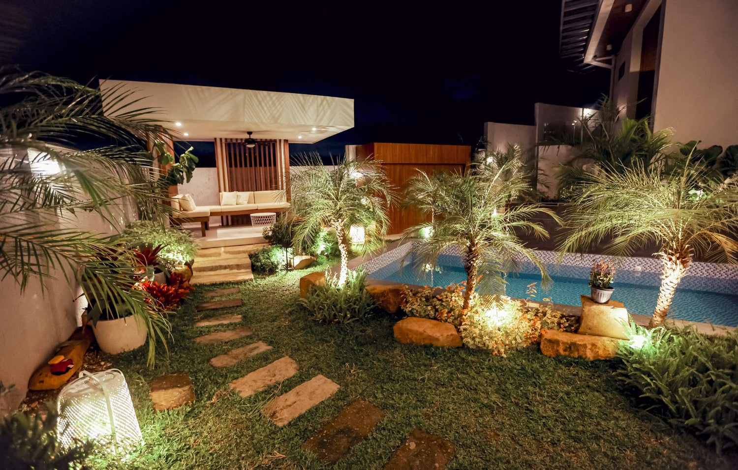  A cozy backyard scene at night, showcasing a glistening pool and swaying palm trees illuminated by soft moonlight.