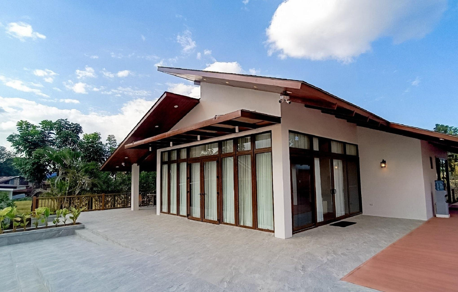 Modern house with large windows, a sloping roof, and spacious front patio under a clear sky.