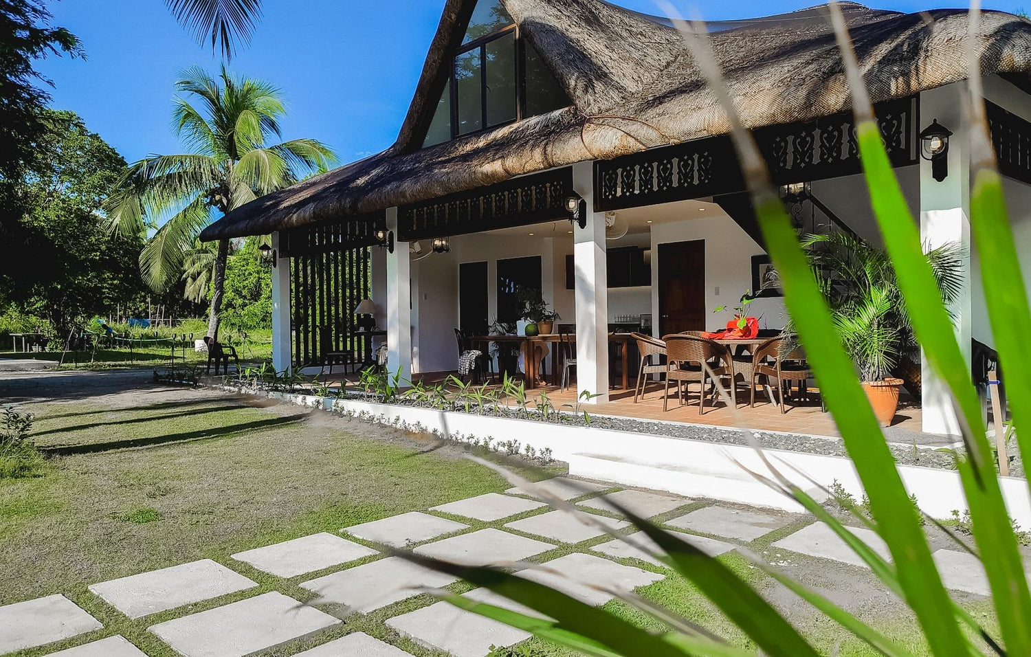 Thatched-roof house with open patio and dining set under a blue sky.