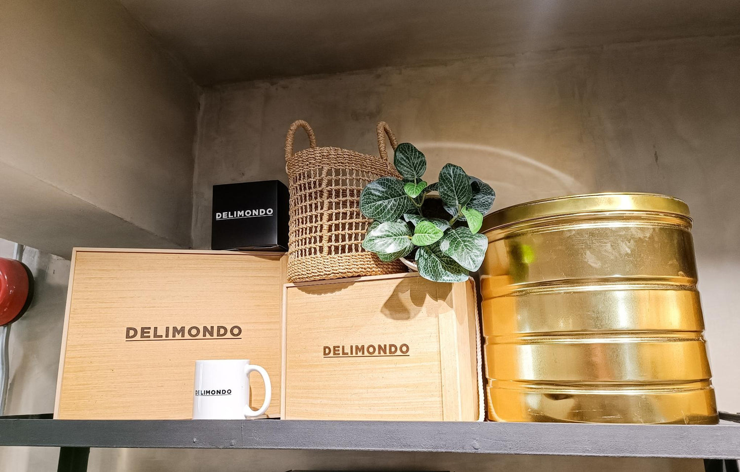 Shelf with Delimondo boxes, a jute bag, green plant, and gold tins.