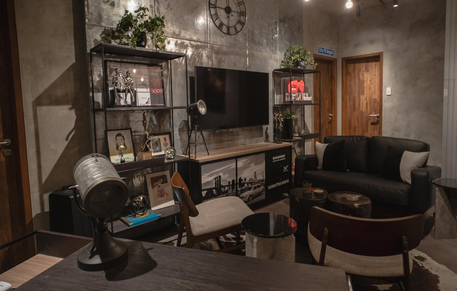 Modern living room with industrial decor, including a large clock, TV, black sofa, and display shelf.