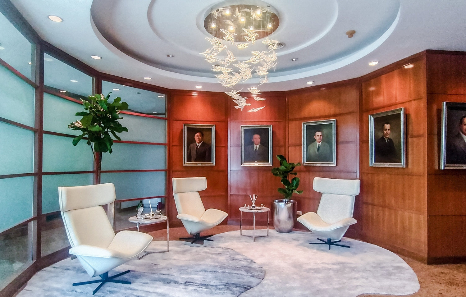 Elegant room with modern chairs, wooden paneling, portraits on wall, and a chandelier.
