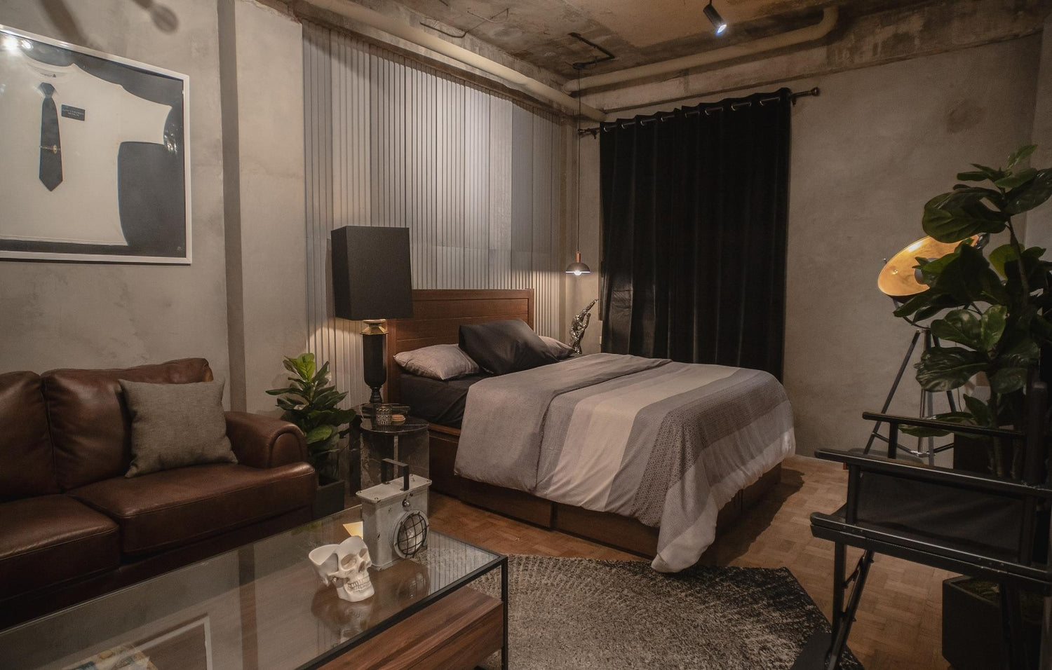 Modern industrial-style bedroom with exposed concrete, leather sofa, and a framed abstract artwork.