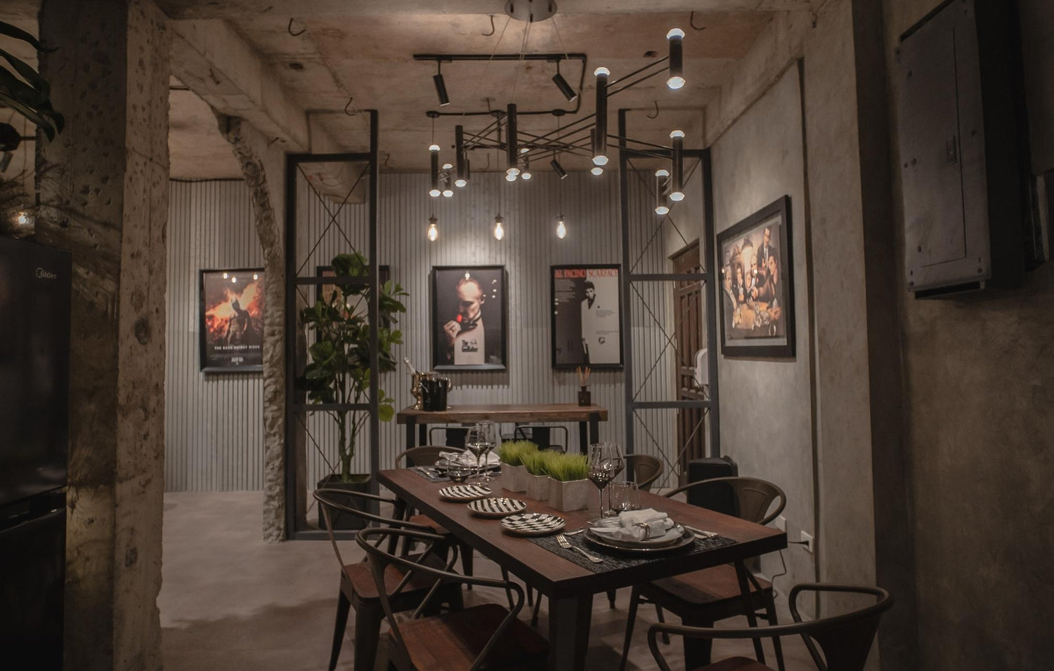 Industrial-style dining room with a dark wood table, hanging lights, and movie posters on the walls.