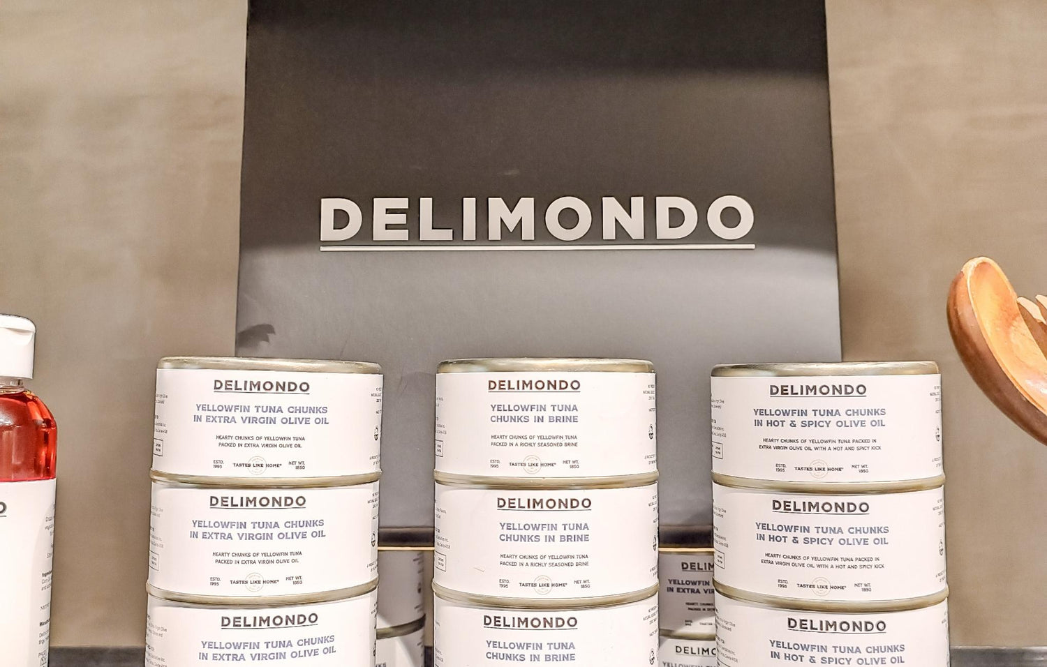 Stacked cans of 'Delimondo' tuna in various flavors in front of a sign with the brand name.