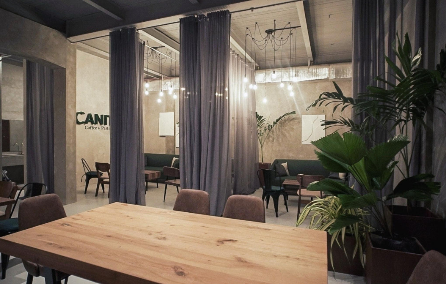 Modern cafe interior with wooden tables, chairs, grey curtains, and potted plants.