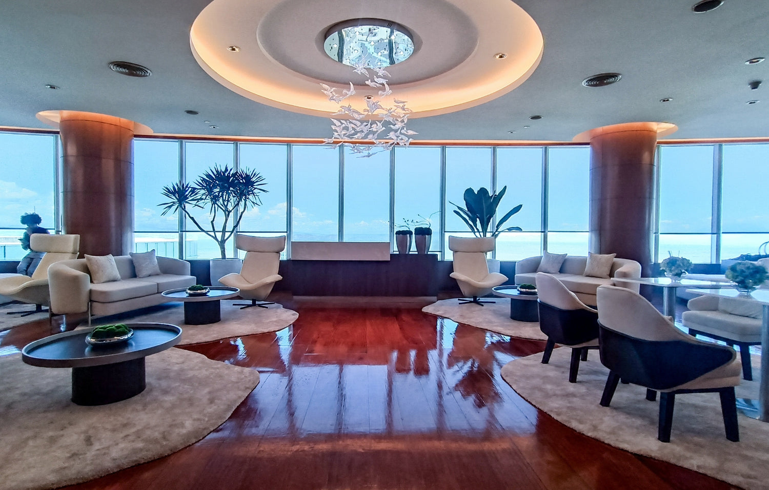 Luxurious interior with round seating, wood floors, large windows overlooking the ocean.
