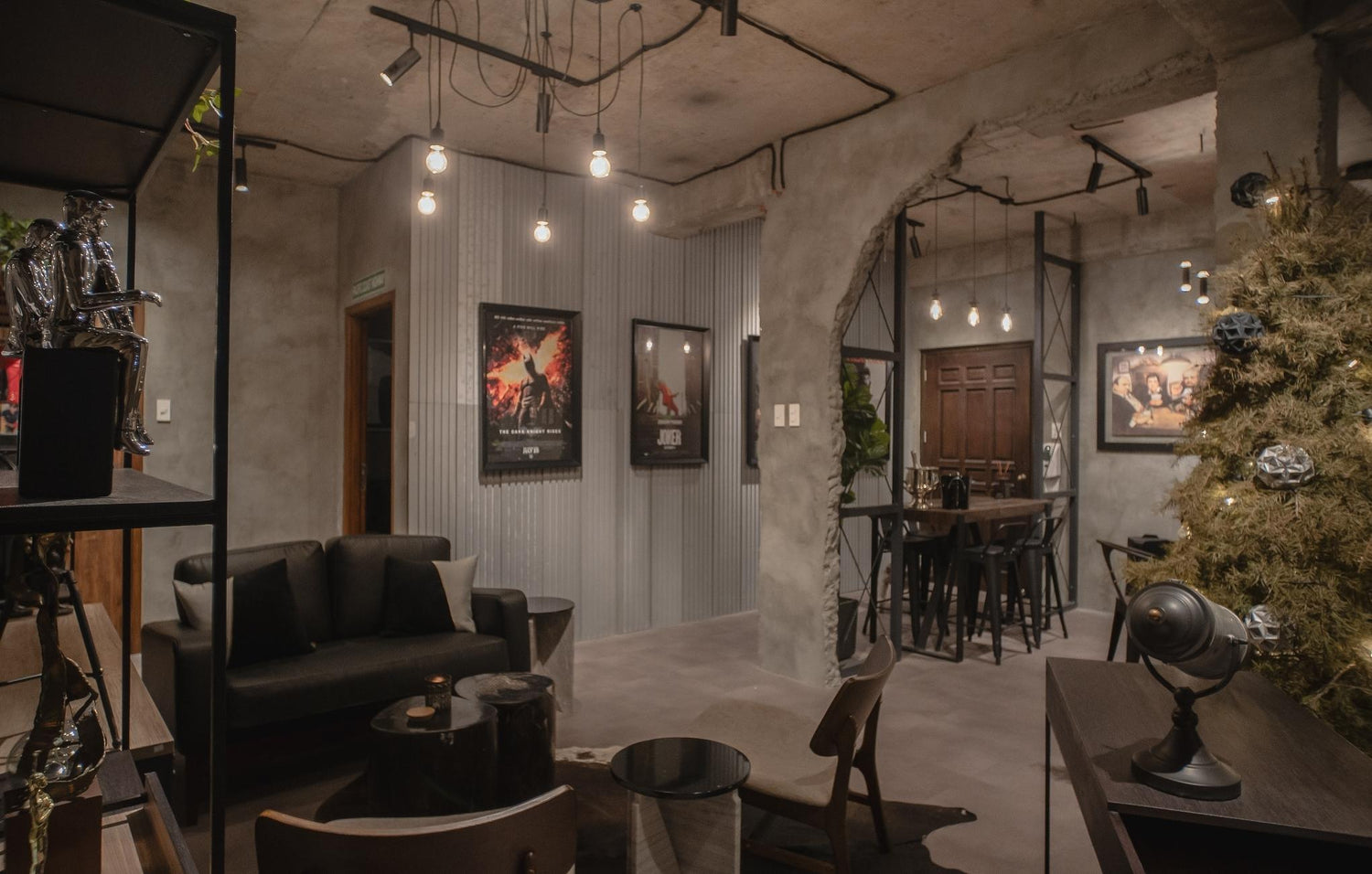 A stylish room with a black sofa, industrial decor, movie posters, and hanging lights.