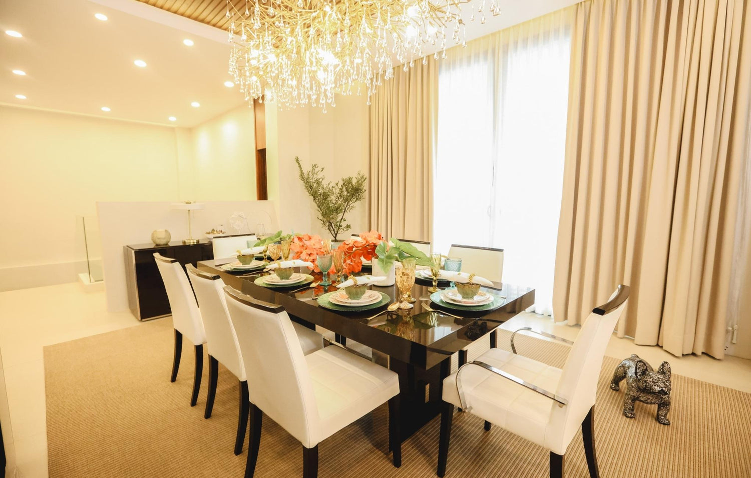 A cozy dining room featuring an elegant chandelier hanging above a beautifully set table.
