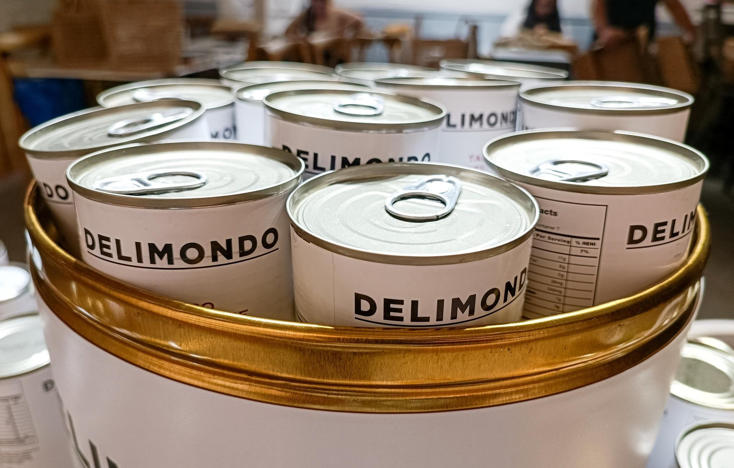 Stacked cans of 'Delimondo' tuna in various flavors in front of a sign with the brand name.