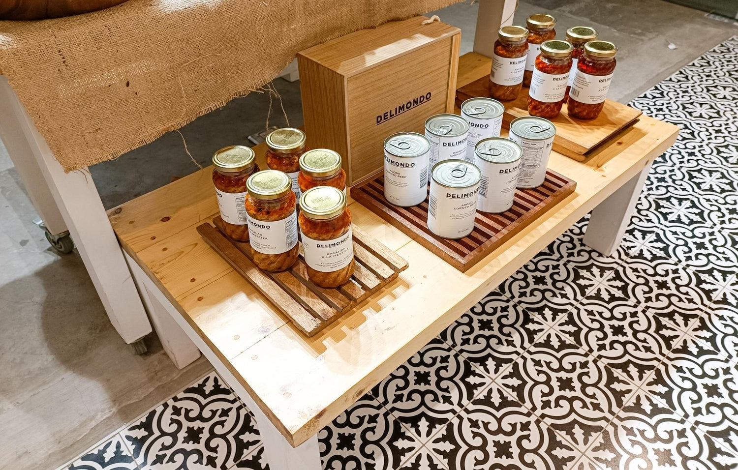 Display of assorted jarred goods on wooden shelves with a decorative floor and label "DELIMONDO."