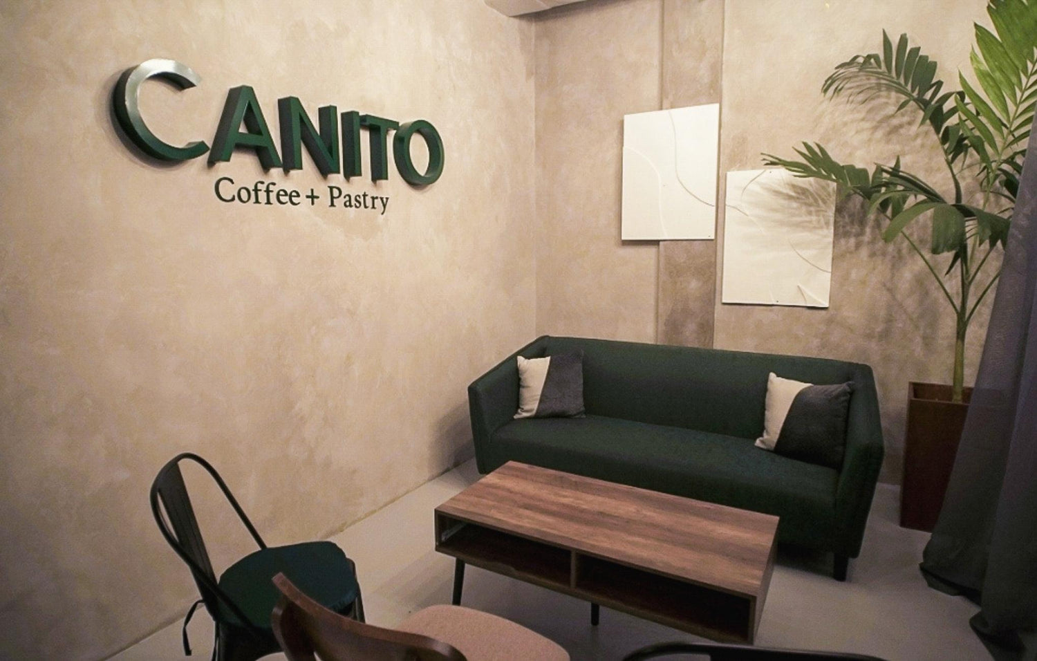 A cozy café corner with a green sofa, wooden table, and "CANITO Coffee + Pastry" sign on the wall.