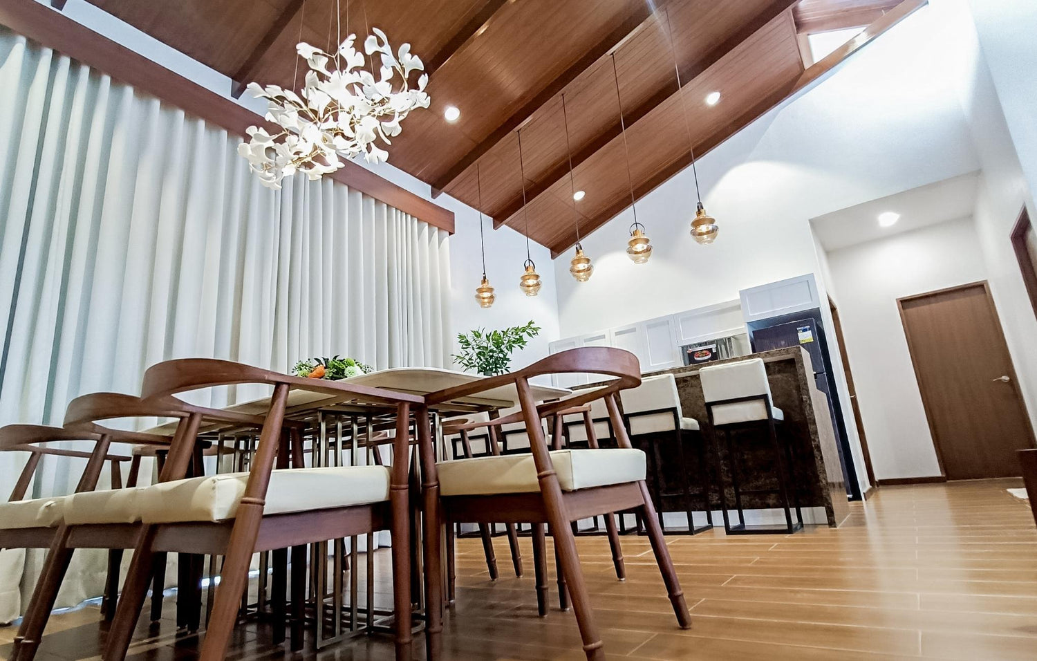 Modern dining room with wooden table, chairs, pendant lights, and a white floral chandelier.